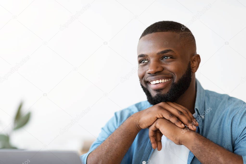 Successful African American freelancer guy sitting at desk with laptop looking aside