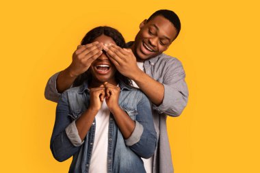 Neşeli siyah adam heyecanlı kız arkadaşını şaşırtıyor, gözlerini arkadan kapatıyor.