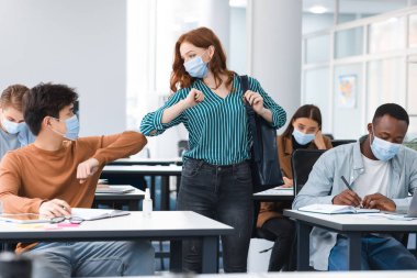 Tek kullanımlık yüz maskeleri takan farklı insanlar selamlıyor ve dirseklerini çarpıştırıyor.
