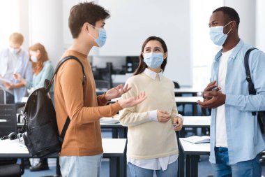 Tıbbi maske takıp konuşan mutlu uluslararası öğrenciler.
