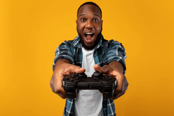 Возбужденный черный парень, играющий в видеоигры Холдинг игровой контроллер в студии