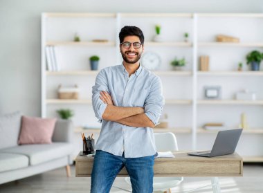 Ev ofisinin masasında kameraya poz verip gülümseyen mutlu, bağımsız Arap adam.