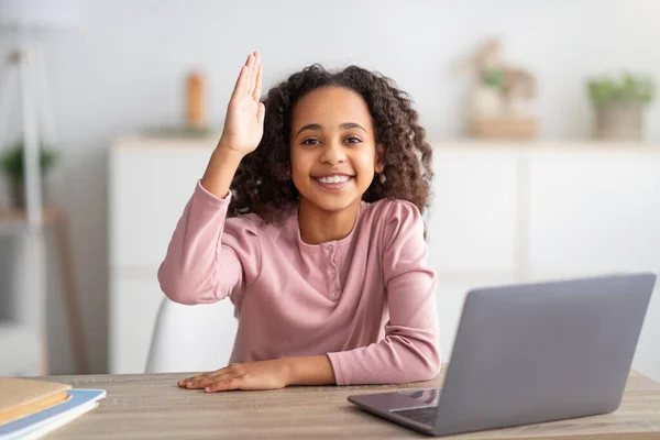 Distant education. Black schoolgirl at laptop raising hand during online school class