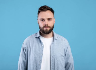 Mavi stüdyo arka planındaki kameraya bakan ciddi bir gencin portresi.