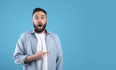 İnanılmaz bir haber. Genç sakallı adam şok içinde ağzını açıyor, mavi stüdyo arka planındaki boşluğu işaret ediyor.