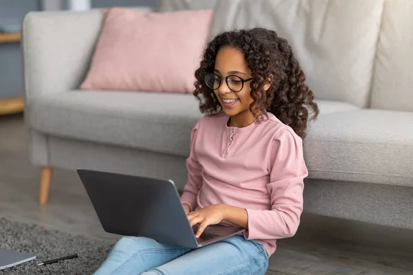 E-learning concept. African american gen z girl using her laptop, doing homework, watching online course at home