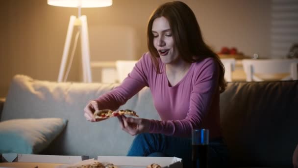 周末的消遣。年轻快乐的女人在送外卖时吃着火辣的披萨，晚上呆在家里看电视 — 图库视频影像