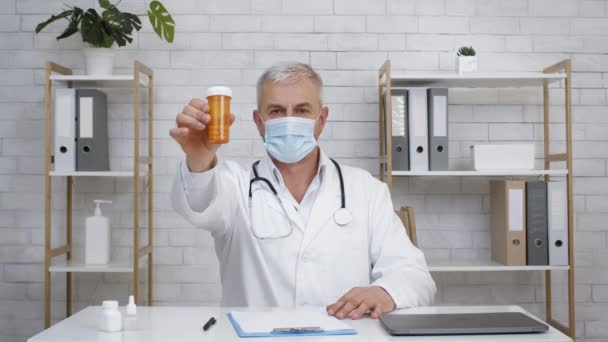 Médico con máscara facial mostrando píldoras Tubo de publicidad de medicamentos en interiores — Vídeos de Stock