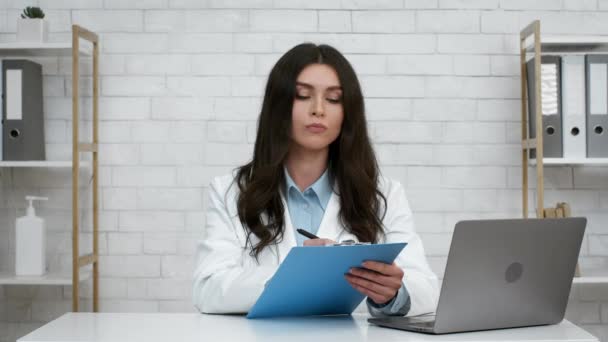 Médico feminino tomando notas e cabeça de aceno sentado no escritório — Vídeo de Stock