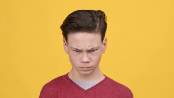 Dühös tini fiú ráncolja a szemét a kamera felett sárga háttér — Stock videók