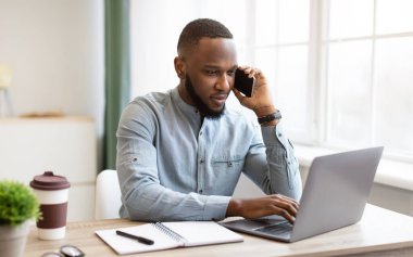 Ciddi bir Afrikalı iş adamı iş yerinde telefonda konuşuyor.