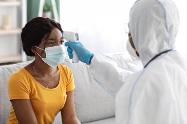 Takım elbiseli hemşire koronavirüs semptomu için kadın sıcaklığını kontrol ediyor.