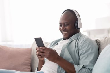 Rahat orta yaşlı Afro-Amerikalı adam akıllı telefondan kablosuz kulaklıkla müzik dinliyor.