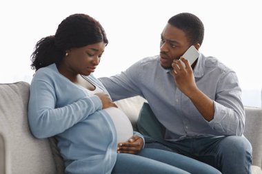 Endişeli siyahi adam doktoru ararken karısı da karın ağrıları çekiyor.