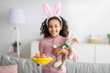 Tatlı Paskalya tavşanı. Süslü yuvada parlak renkli yumurtalar tutan mutlu siyah kız.