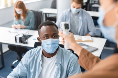 Temassız termometre tabancası olan öğretmen, siyah öğrencinin sıcaklığını ölçüyor.