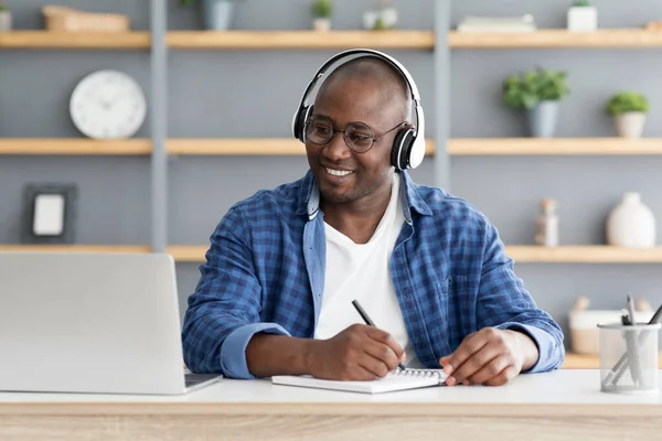 E-educação. Homem maduro preto feliz usando laptop e tomar notas, ouvindo curso on-line — Fotografia de Stock