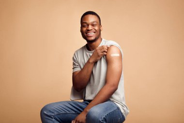 Covid-19 Vaccinated African Man Showing Arm With Plaster, Beige Background clipart