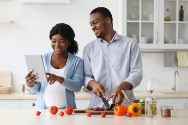 Smiling black pregnant couple using digital tablet in kitchen