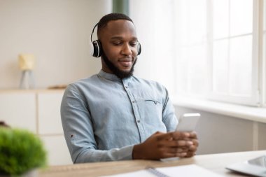 İş yerinde akıllı telefon kullanan rahat siyahi işadamı kulaklık takıyor.