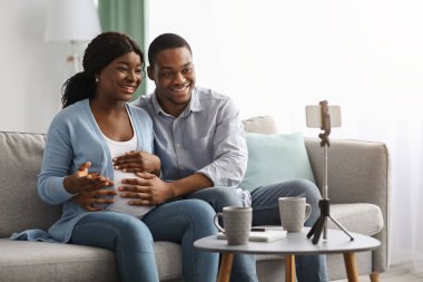 Gülümseyen Afrikalı Amerikalı bir adam ve hamile bir kadın video görüşmesi yapıyorlar.