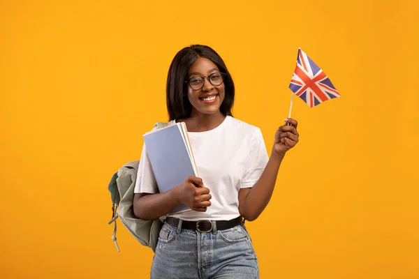 Positive black woman student with backpack holding UK flag