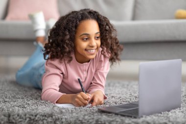 E-öğrenme. Mutlu kız evde ders çalışıyor ve dizüstü bilgisayarın önünde notlar alıyor.