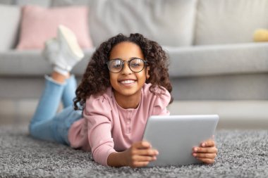 Mutlu yurttaşlar dijital tablet kullanıyor, halıya uzanıyor ve kameraya gülümsüyor.