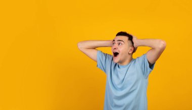 Havalı genç adam şok içinde başını tutuyor, çığlık atıyor ve turuncu stüdyo arka planında boş bir alana bakıyor.