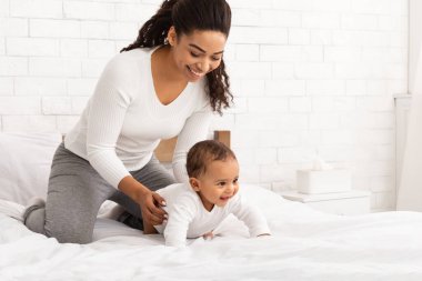 Siyah Anne, bebek bebekle oynuyor. Yatakta emekliyor.