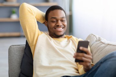 Siyah adamın kanepede oturup akıllı telefon kullandığı yakın plan.