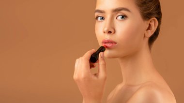 Güzel genç bayan ruj sürüyor, kahverengi arka planda görünüşüne özen gösteriyor, kopya alanı olan bir panorama.
