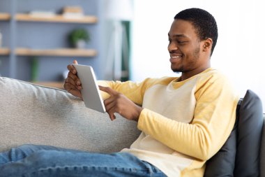 Dijital tablet kullanarak koltukta dinlenen mutlu Afro-Amerikalı adam.