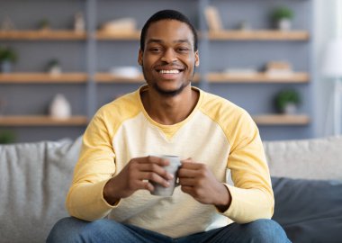 Rahatlamış yakışıklı siyah adam oturma odasında kahve içiyor.