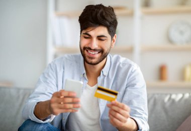 Çevrimiçi alışveriş. İnternet 'ten ürün sipariş etmek için telefon ve kredi kartı kullanan mutlu bir Arap.