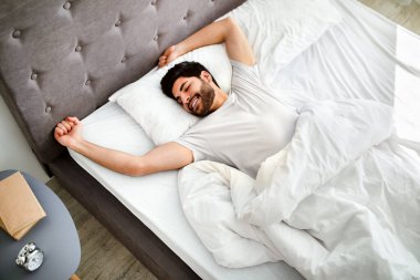 Rahat bir uyku. Mutlu dinlenmiş Arap adam uyanıyor, yatakta ellerini uzatıyor ve gözleri kapalı gülümsüyor..