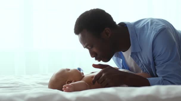 Amor y ternura. Cuidar al padre afroamericano jugando con su bebé recién nacido, acostado en la cama en casa, espacio vacío — Vídeo de stock