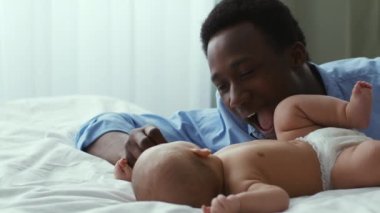 Samimi baba sevgisi. Mutlu Afrikalı Amerikalı adam yeni doğmuş bebeğiyle oynuyor, evde yatakta yatıyor.