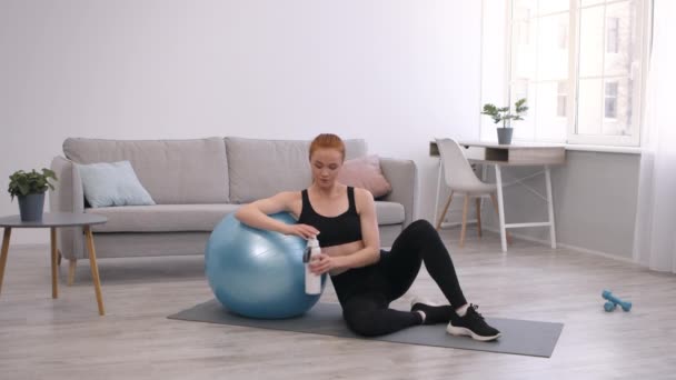 Mujer agua potable sentada cerca de Fitball durante el entrenamiento en casa — Vídeos de Stock