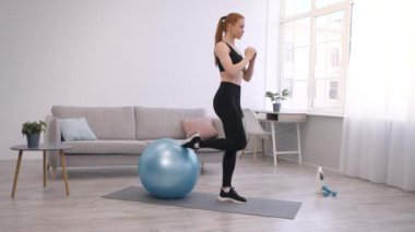 Spor kadını evde spor yaparken tek bacaklı çömelmeler yapıyor.