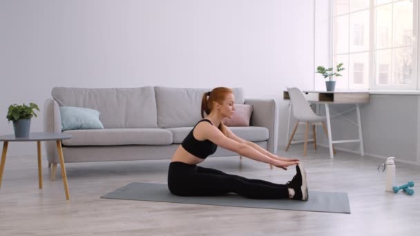 Mujer Fitness haciendo estiramientos de tendones de isquiotibiales sentada en el suelo en casa — Vídeos de Stock