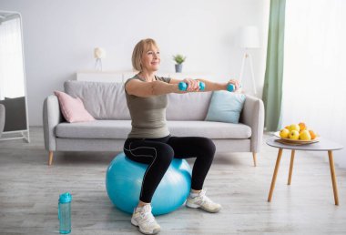 Güçlü, olgun bir kadın evde spor yaparken halterlerle spor yapıyor.