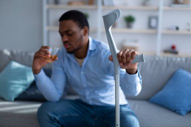 Sakatlığı yüzünden koltuk değneği olan siyah bir adam evde acısını dindirmek için alkol alıyor.