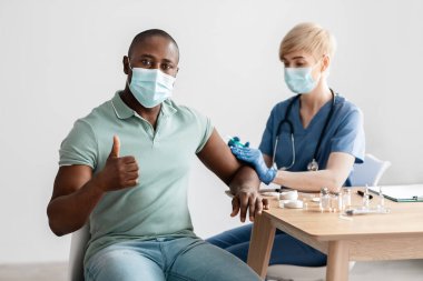 Koruyucu maskeli ve üniformalı olgun kadın doktor. Bin yıllık Afro-Amerikan erkek aşısı.