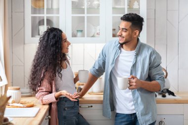 Neşeli Orta Doğulu çift mutfakta dinleniyor, kahve içiyor ve sohbet ediyorlar.