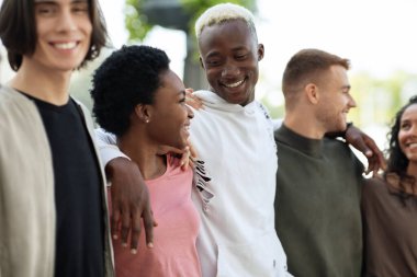 Mutlu arkadaşlar sokakta yürüyorlar, sarılıyorlar ve konuşuyorlar.