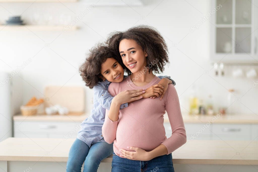 African American girl hugging her pregnant mum from the back