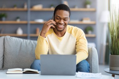 Gülümseyen siyah adam evde akıllı telefondan konuşuyor.