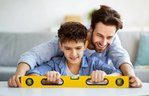 Happy father teach son using level tool for measure surface, doing apartment repair together themselves