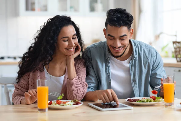 Online Shopping. Happy Arab Spouses Using Digital Tablet During Breakfast In Kitchen